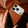 Hand holding a brown leather iPhone case with textured finish and raised camera protection