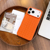 Orange braided iPhone case with textured finish displayed on a wooden tray beside magazines