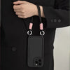 Black iPhone case with pink crossbody strap detail, worn as a hands-free accessory.